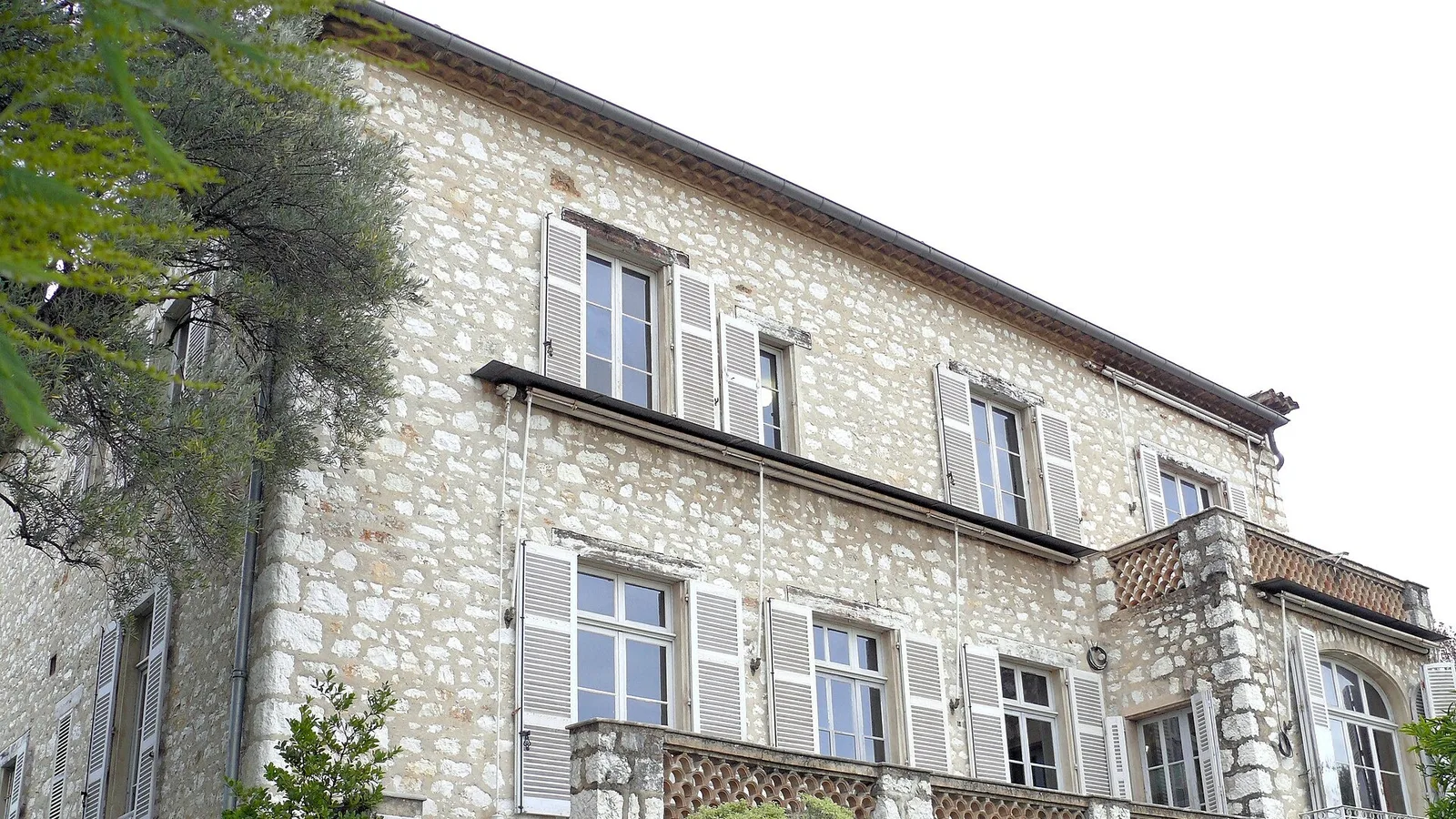 Açık renkli taş duvarlu iki katlı eski Avrupa binası, pencereleri ve sarmaşık.