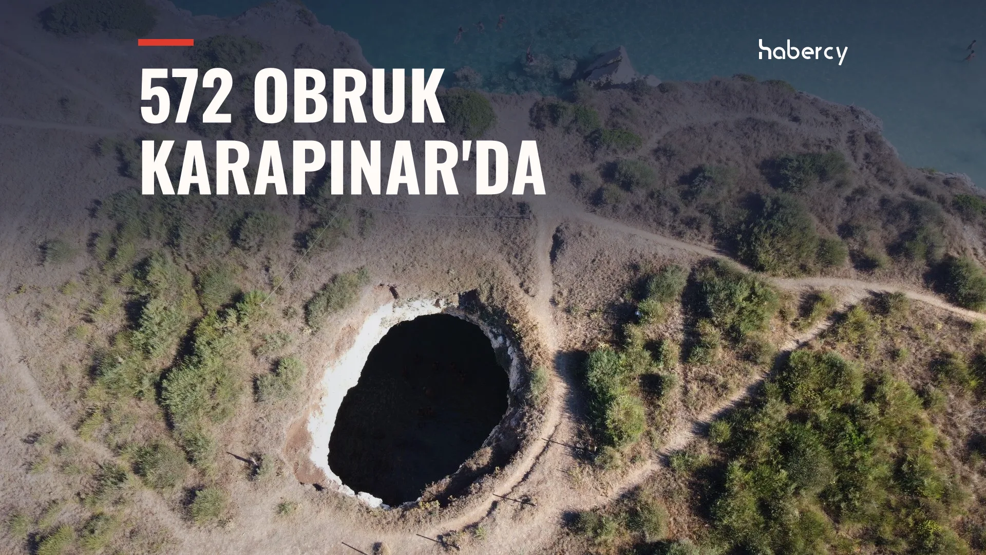Kuru, çalılık bir arazide derin ve yuvarlak bir çukurun havadan görünümü, üst kısımda deniz
