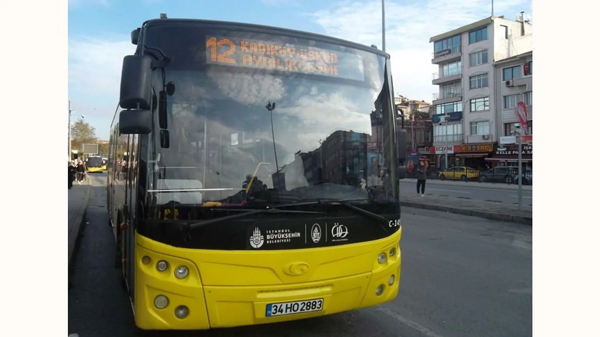 Şehir caddesinde duran, ön camında 12 numaralı hat tabelası bulunan sarı İETT otobüsü