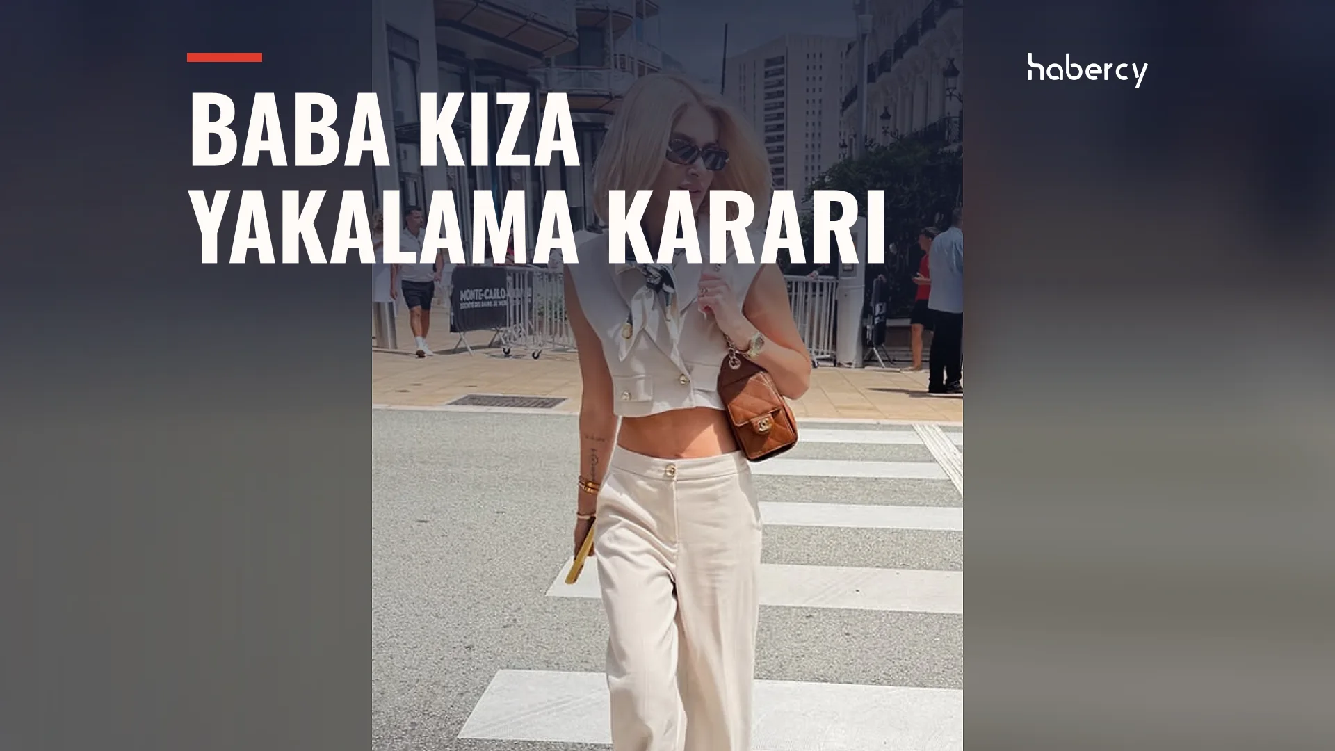 Güneş gözlüklü sarışın kadın, krem pantolon ve yelekle yaya geçidinde yürüyor.