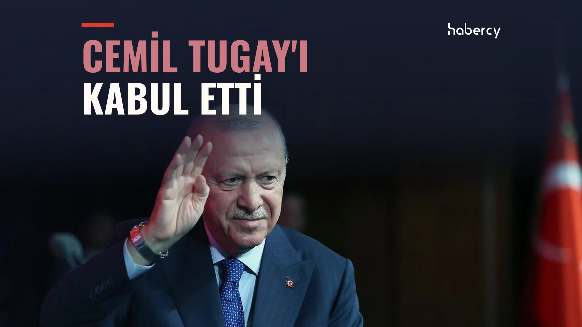 Lacivert takım elbiseli, beyaz sakallı bir adam el sallıyor; arkada Türk bayrağı var