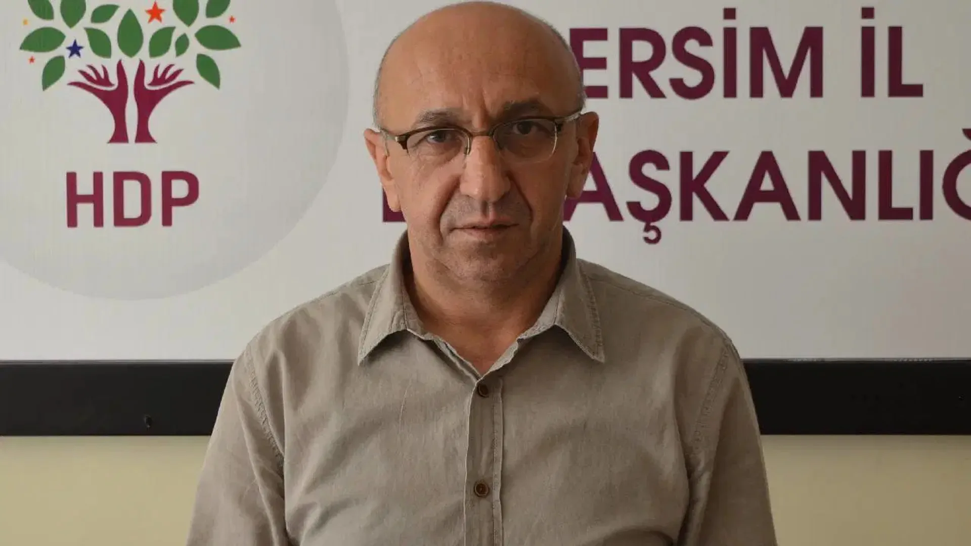 HDP Dersim İl Başkanlığı panosu önünde gözlüklü, gri gömlekli kel bir adam