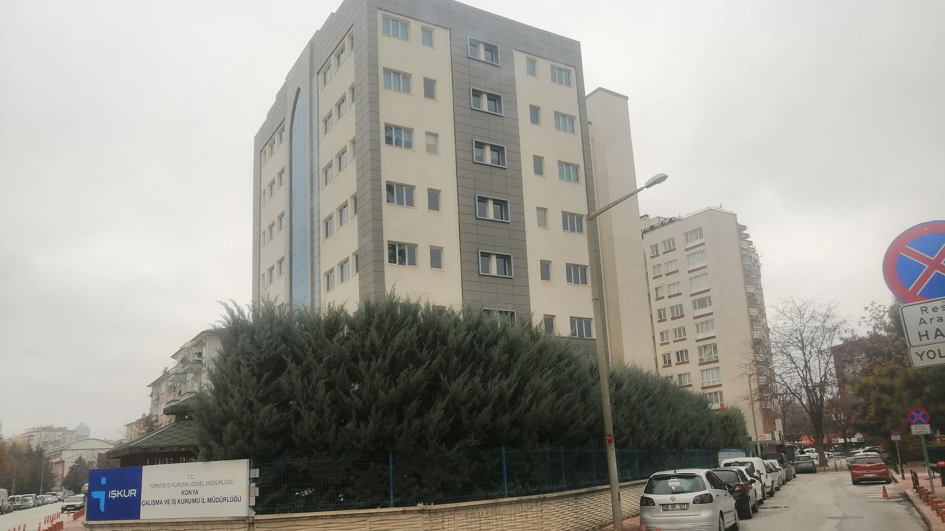Kapalı havada, önünde servi ağaçları olan çok katlı bir bina