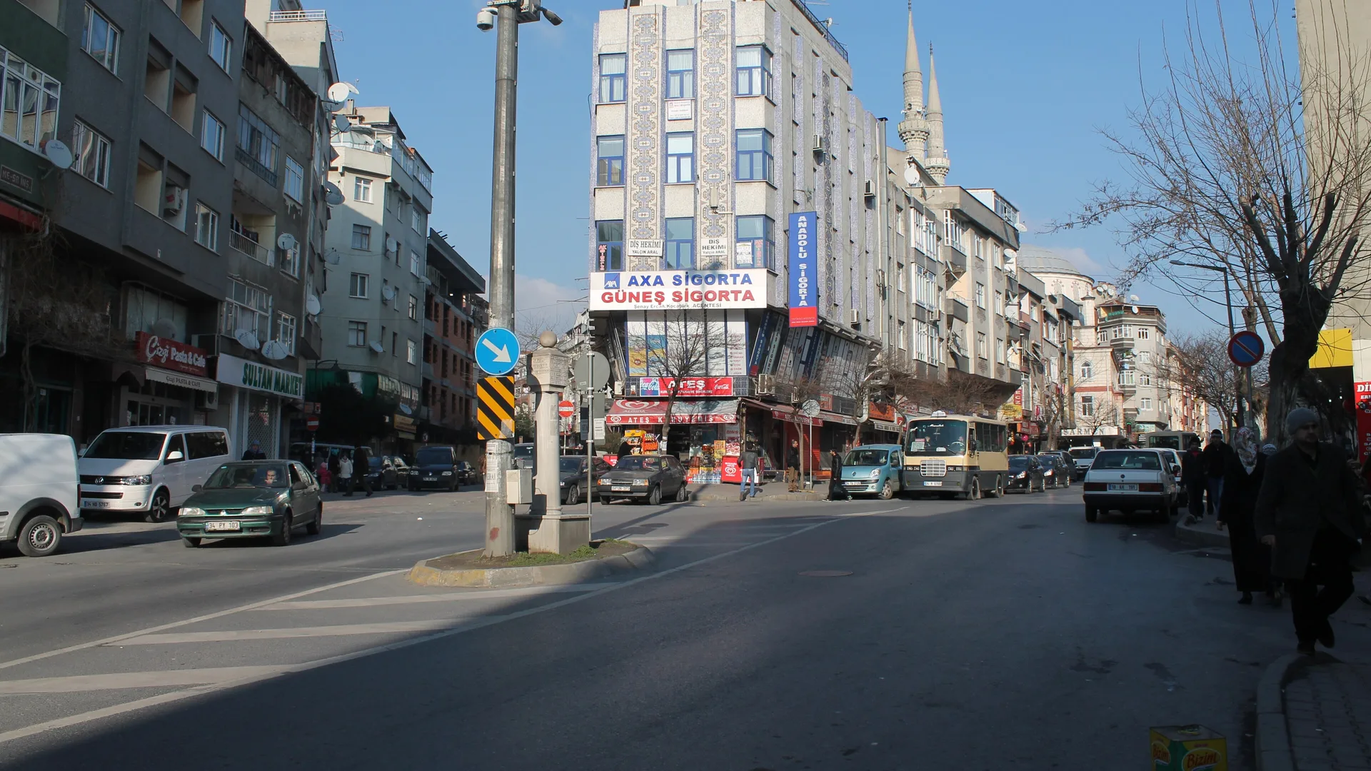 Apartmanlar, dükkânlar ve minareler arasında araçların geçtiği geniş bir cadde