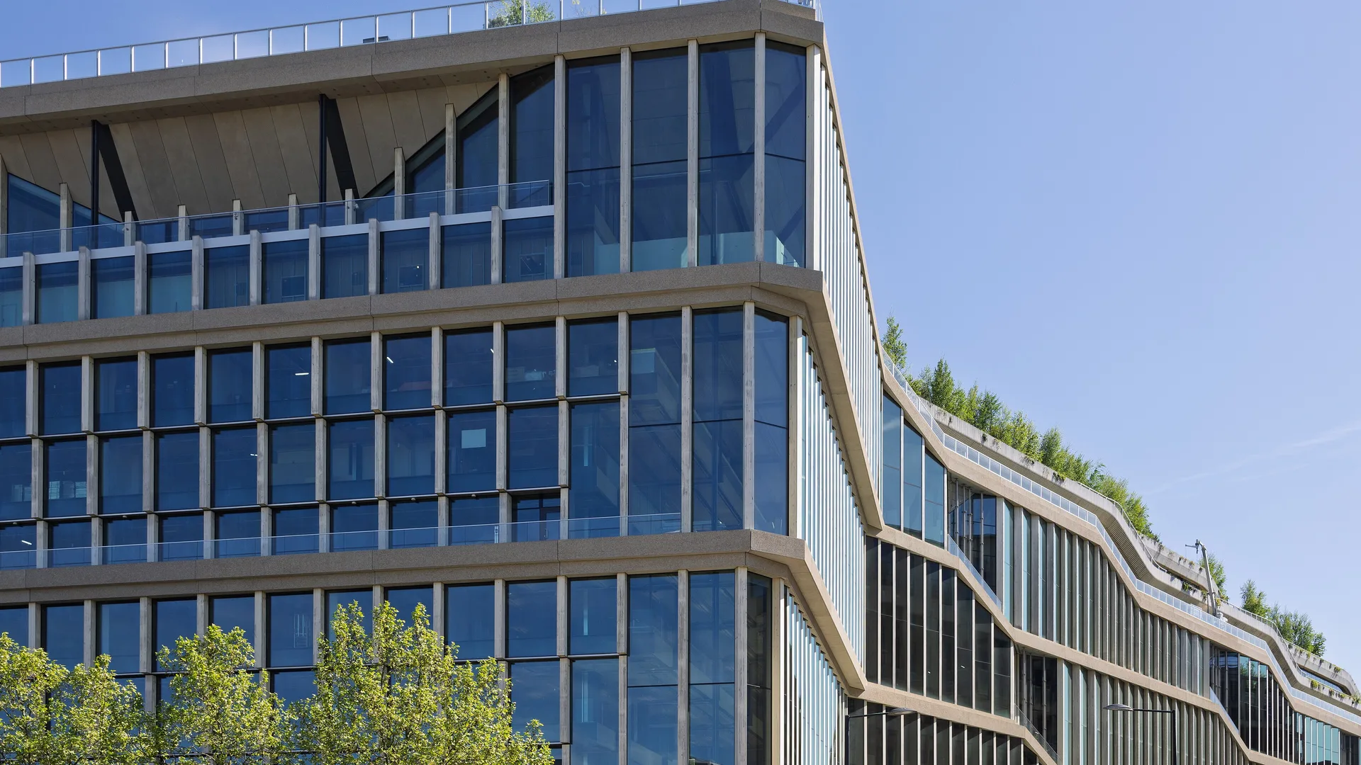 Ağaçların ardında yükselen, çatısı yeşillendirilmiş camlı modern bir ofis binası