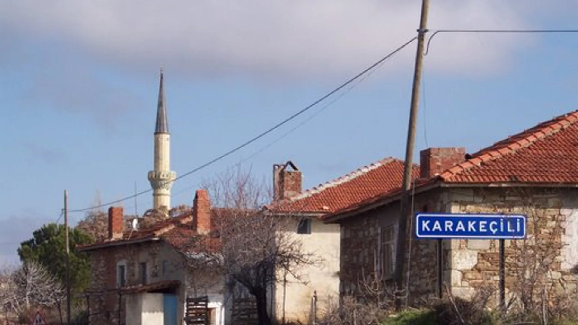 Karakeçili tabelası, kiremit çatılı taş evler, minare ve köy yolu