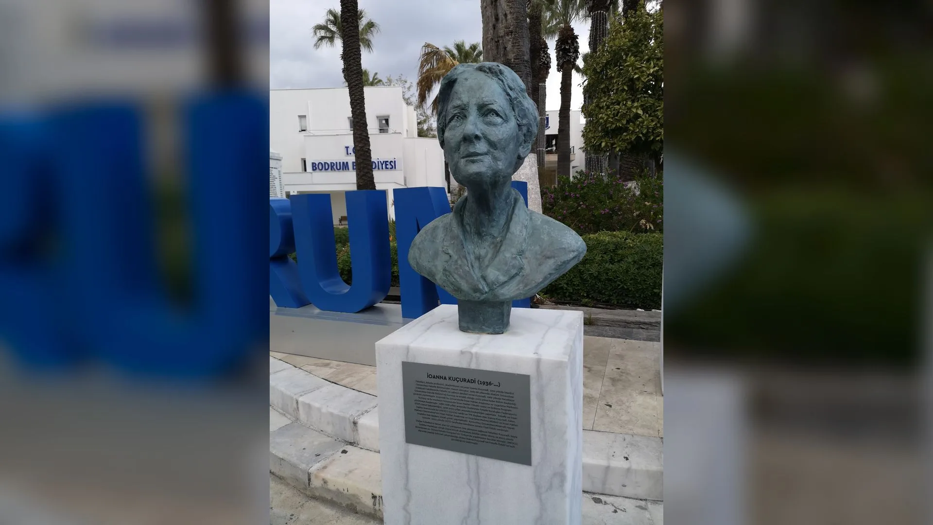 Bodrum Belediyesi önünde, mermer kaide üzerinde yaşlı bir kadının bronz büstü ve yazılı plaket