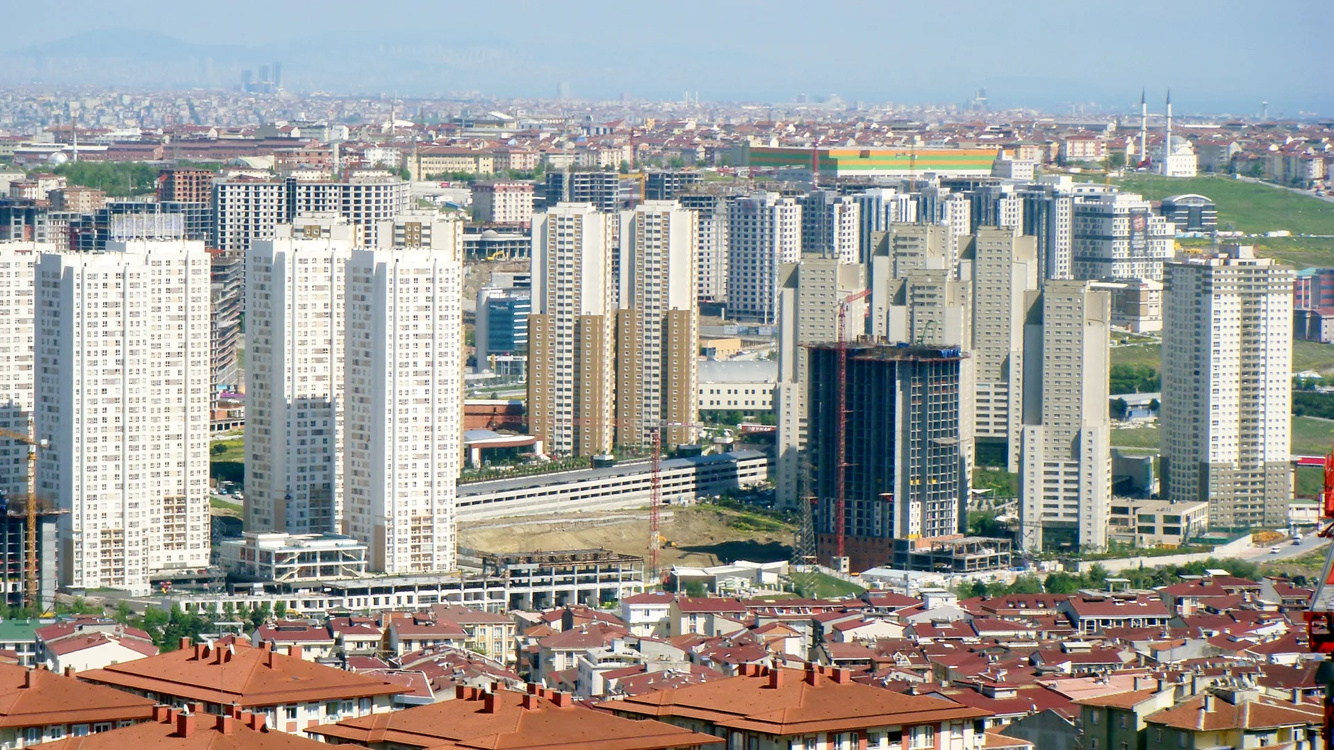 Kırmızı çatılı evlerin ardında yükselen çok sayıda beyaz gökdelen ve inşaat halindeki bir bina