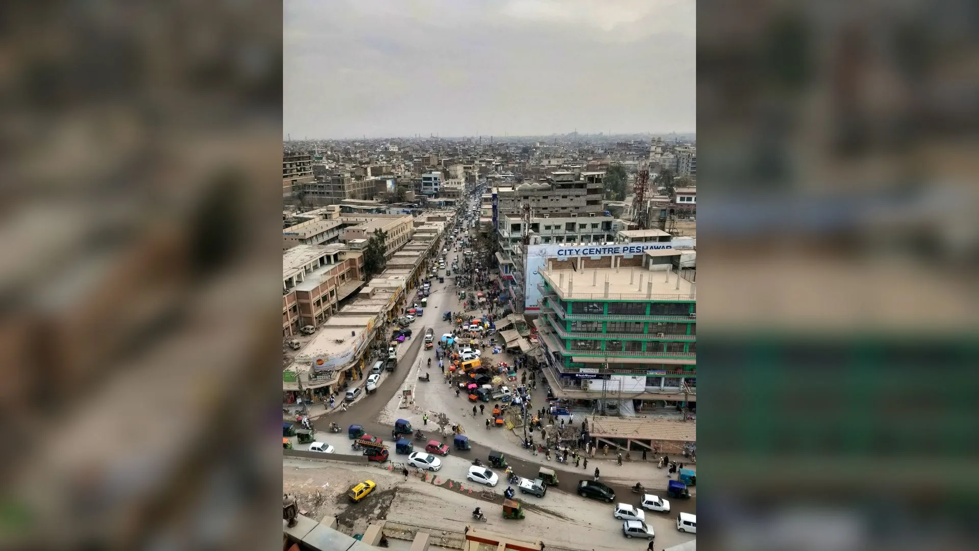 Yüksekten çekilmiş kalabalık bir şehir caddesi, araç trafiği ve City Centre Peshawar tabelalı bina