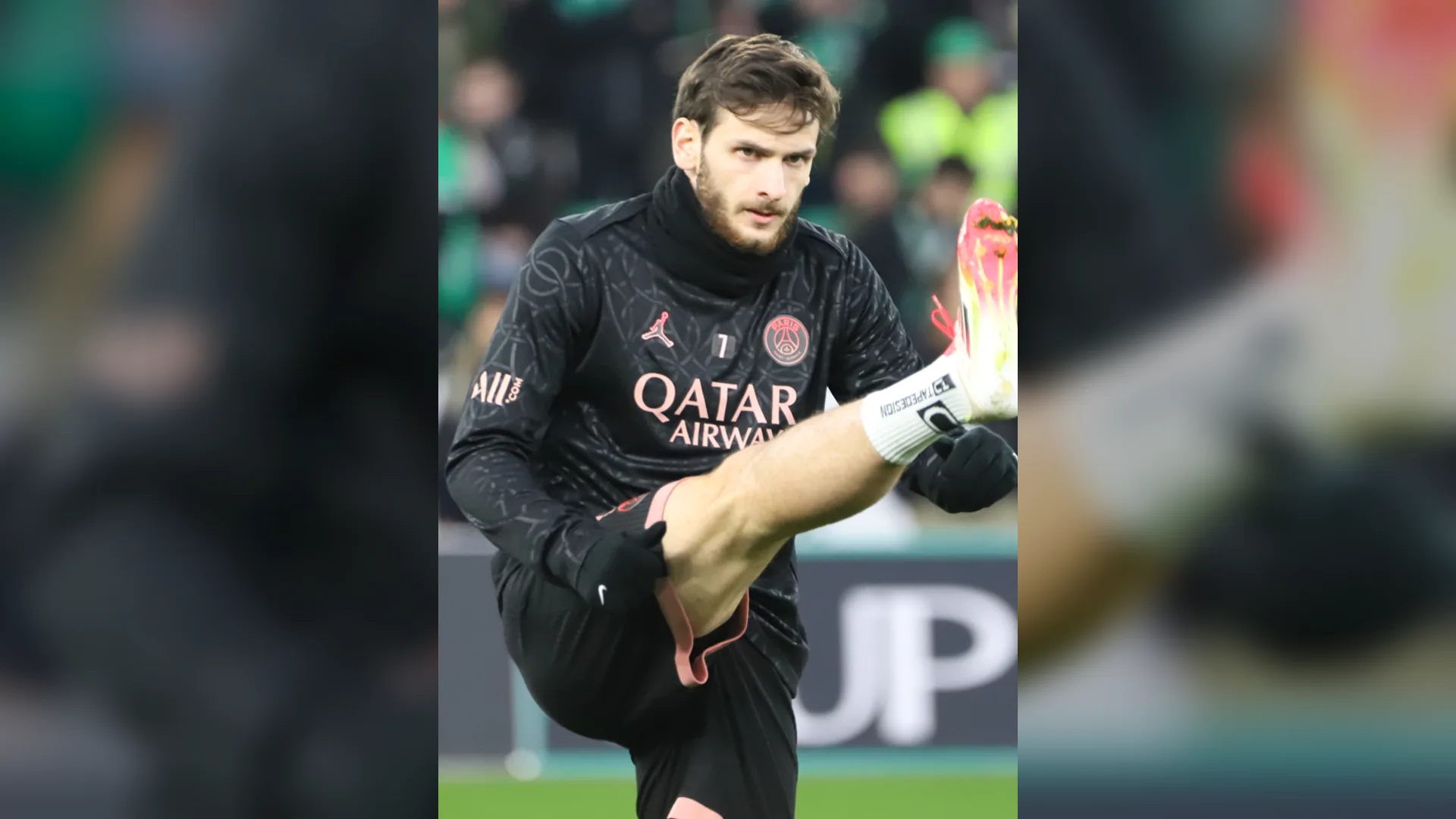 Siyah PSG antrenman üstü giyen sakallı futbolcu, bacağını havaya kaldırarak ısınıyor