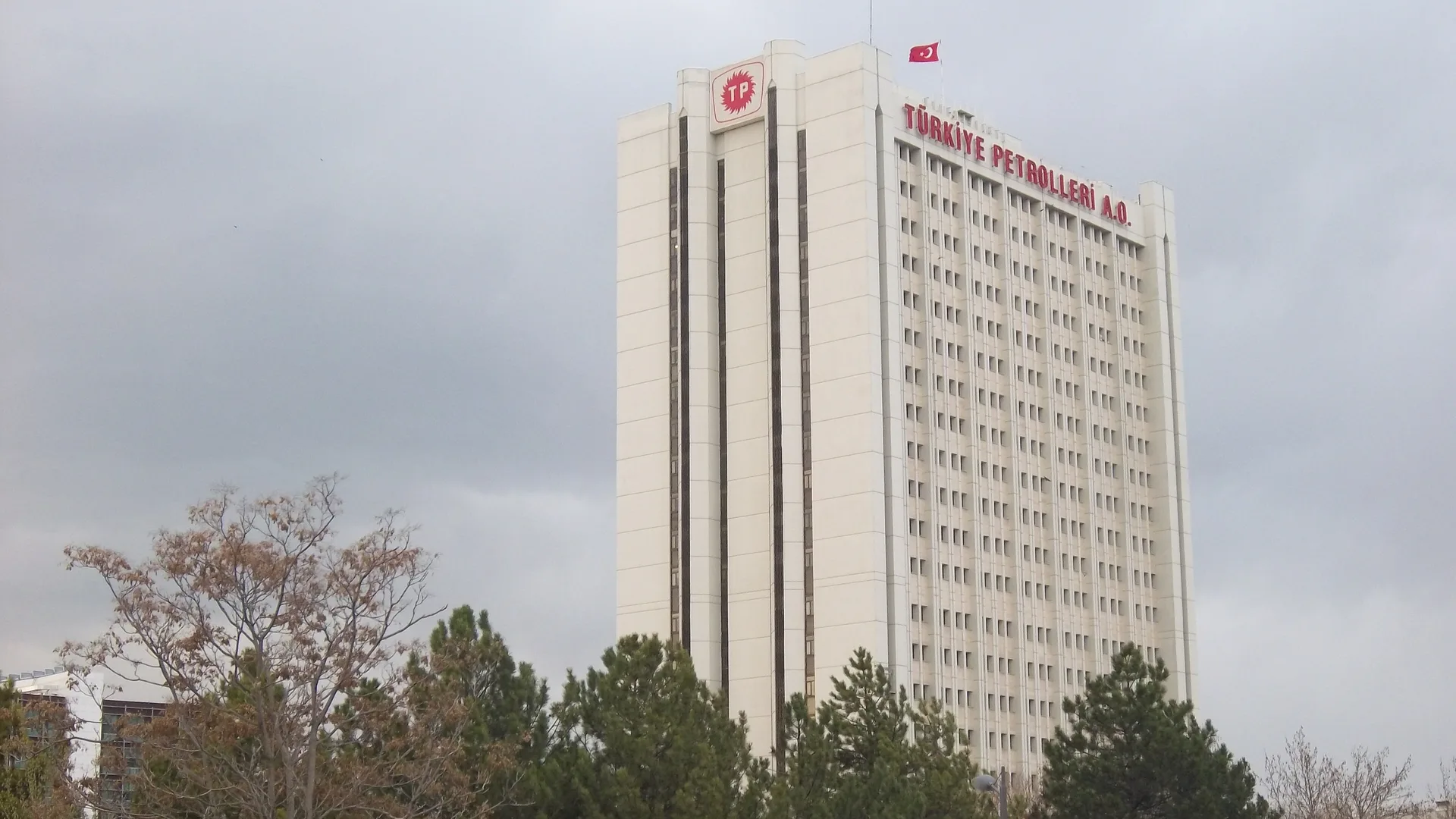 Bulutlu gökyüzü altında üzerinde Türkiye Petrolleri A.O. yazan yüksek beyaz bina ve Türk bayrağı