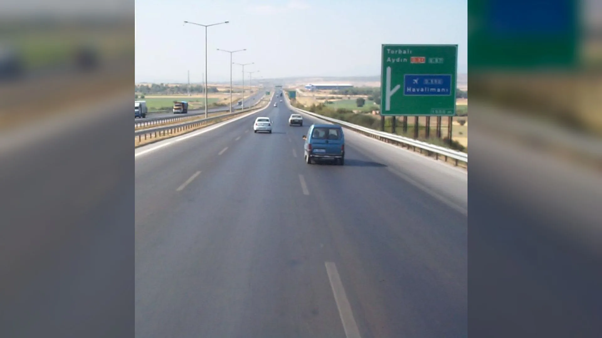 Torbalı ve Aydın yönünü gösteren yeşil tabelalı geniş otoyolda ilerleyen minibüs ve otomobiller
