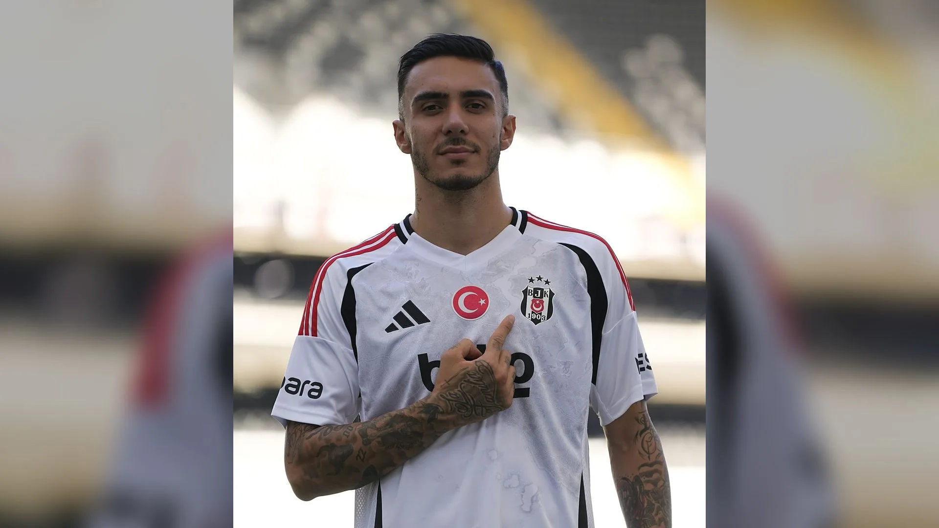 Beyaz Beşiktaş formalı, dövmeli genç futbolcu stadyumda armayı gösteriyor.