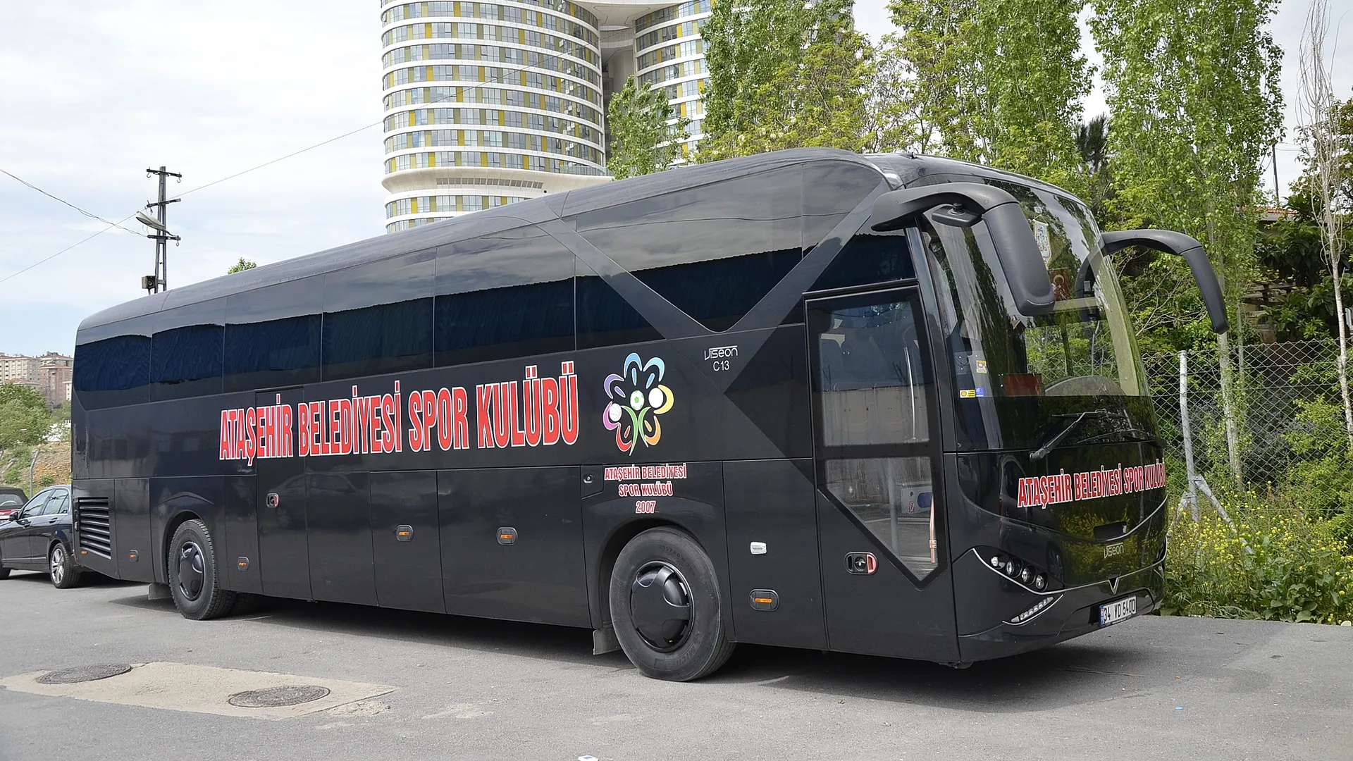 Ataşehir Belediyesi Spor Kulübü yazılı siyah otobüs, arkasında silindir biçimli yüksek bir konut binası