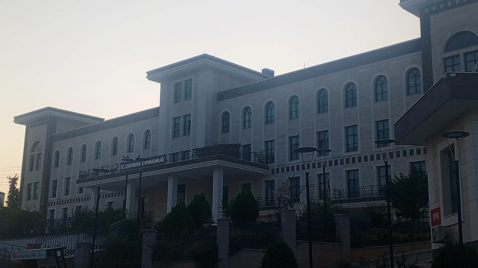 Alacakaranlıkta Çukurova Kaymakamlığı tabelalı, kemerli pencereli çok katlı bej bina