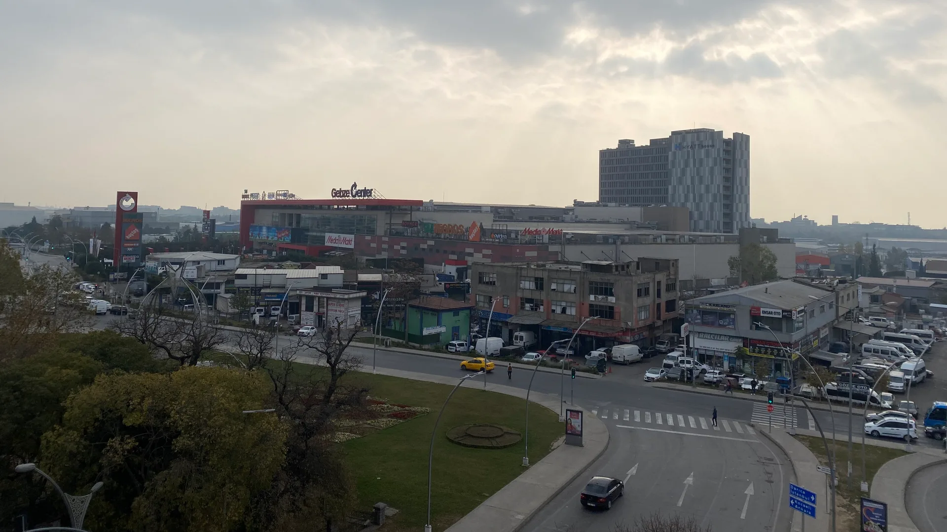 Bulutlu gökyüzü altında Gebze Center AVM, yüksek bir bina ve önünde araçların geçtiği cadde