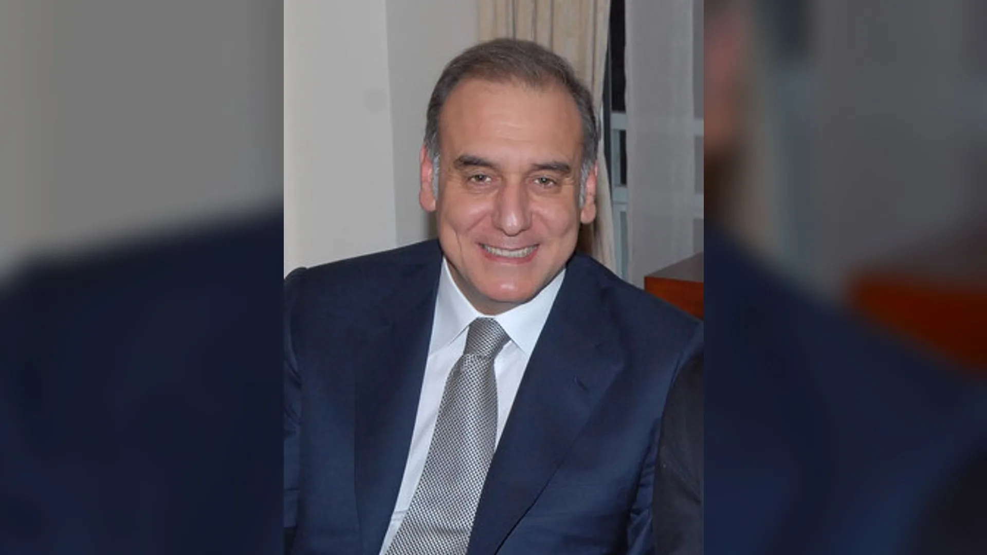 Lacivert takım elbiseli, gri kravatlı, gülümseyen kır saçlı bir adam