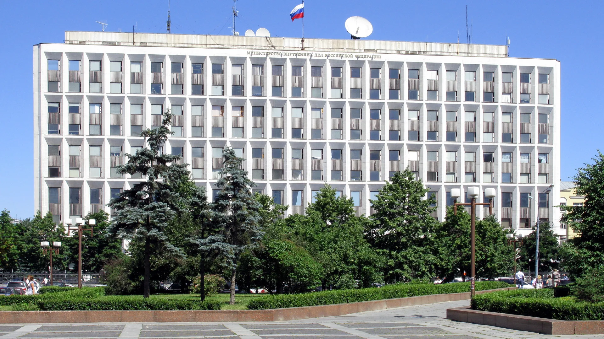 Çatısında Rus bayrağı ve uydu antenleri olan beyaz çok katlı bina, önünde çam ağaçları