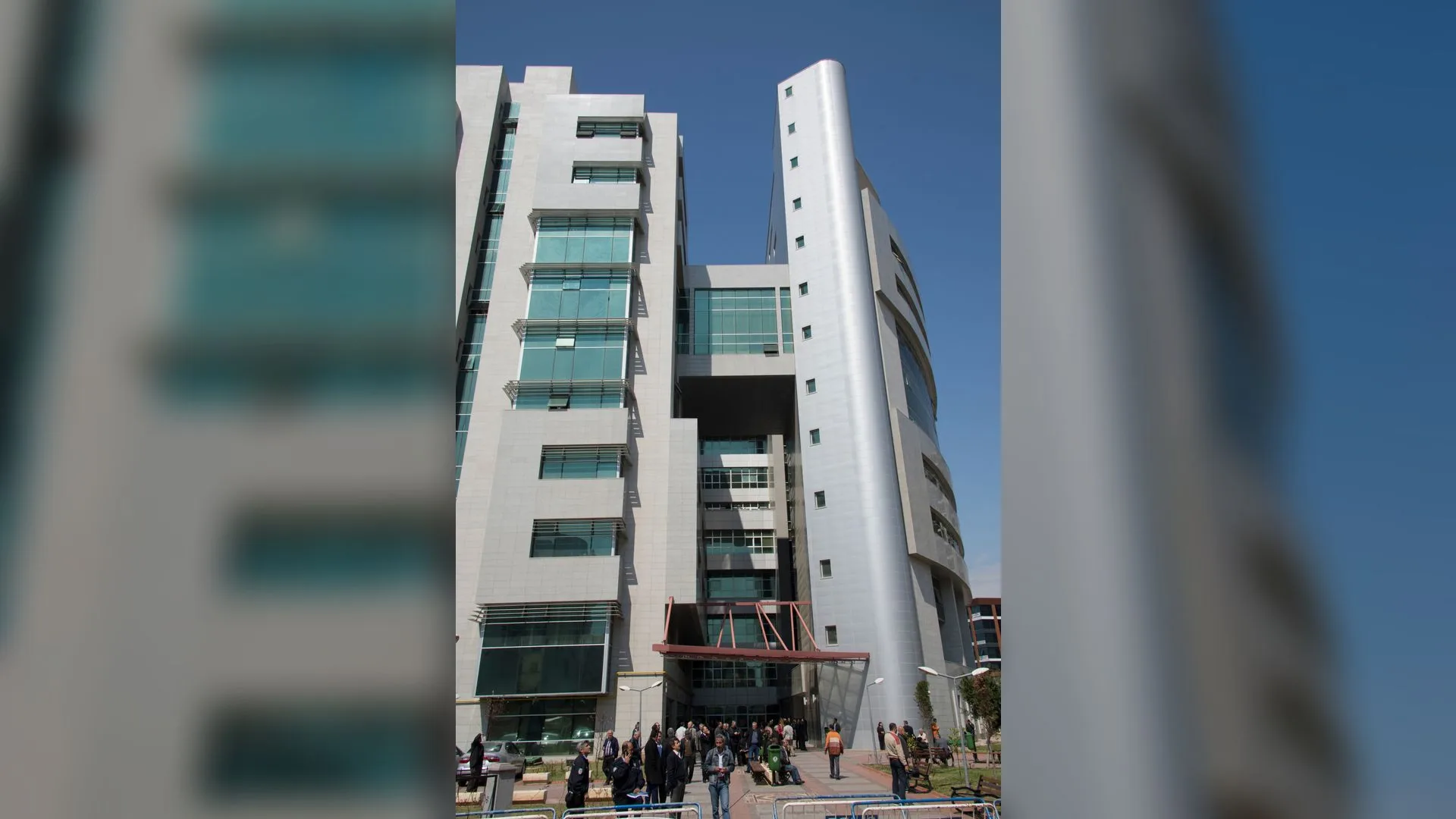 Mavi gökyüzü altında çok katlı modern adliye binası ve önünde bekleyen insanlar