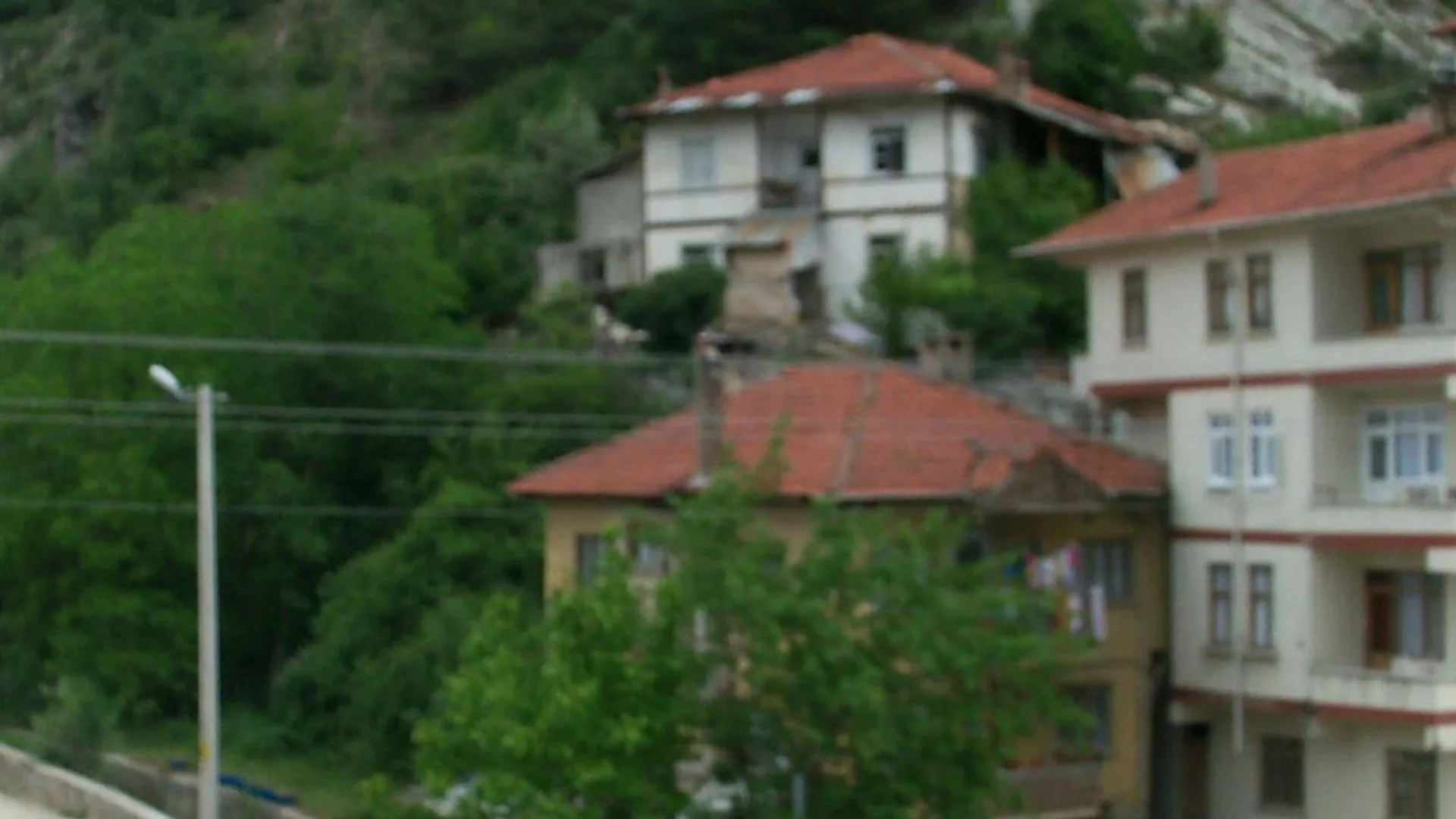 Yeşil yamaç önünde kiremit çatılı beyaz ve pembe evler