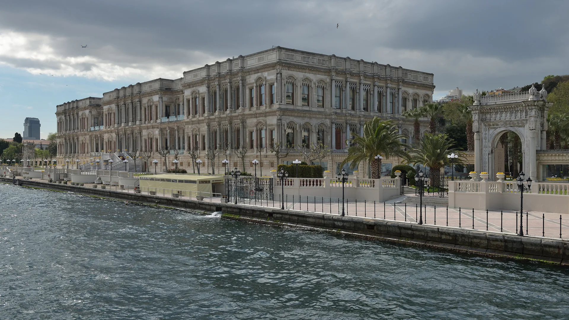Bulutlu gökyüzü altında Boğaz kıyısındaki tarihi saray ve süslü taş kapı