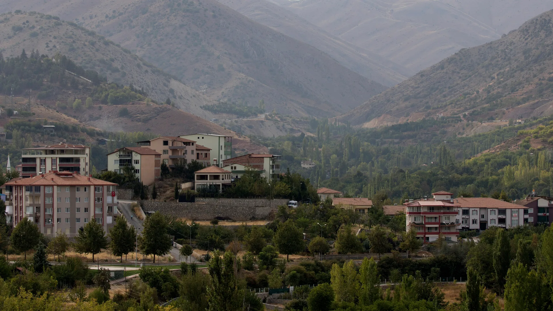 Dağların eteğinde kırmızı çatılı apartmanlar ve yeşil ağaçlarla kaplı bir vadi.