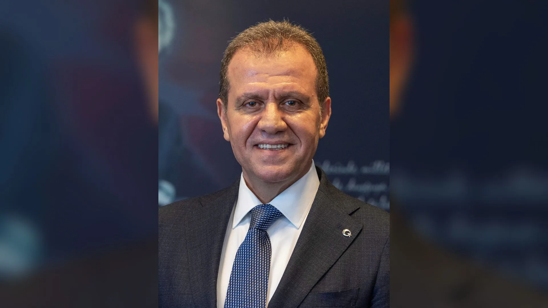 Lacivert takım elbiseli ve mavi kravatlı, gülümseyen kısa saçlı bir adam