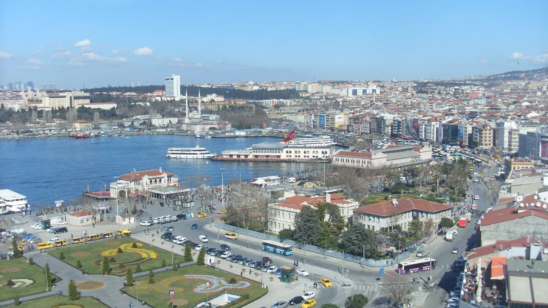 Kadıköy iskele meydanı, deniz kıyısındaki vapur iskeleleri, parklar ve yoğun şehir yapılaşmasının yukarıdan görünümü.