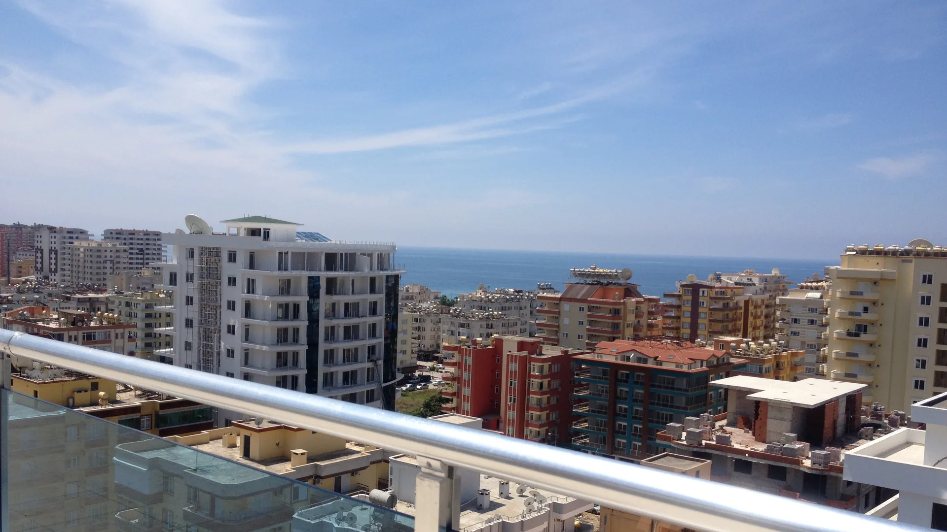 Cam korkuluklu bir balkondan çok katlı apartmanlar ve uzaktaki deniz manzarası