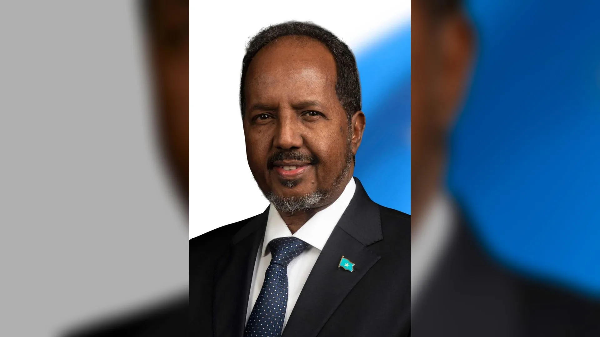 Takım elbiseli, yakasında Somali bayrağı rozeti olan gülümseyen sakallı bir adam