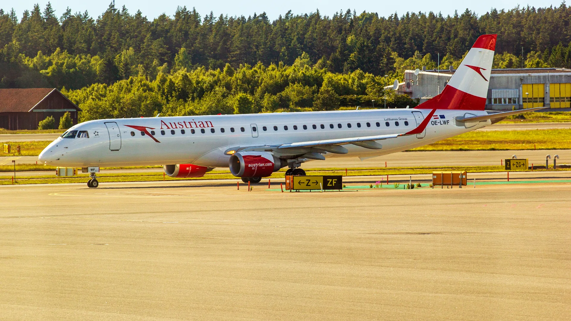 Pistte, ormanlık bir alanın önünde duran beyaz-kırmızı Austrian Airlines yolcu uçağı