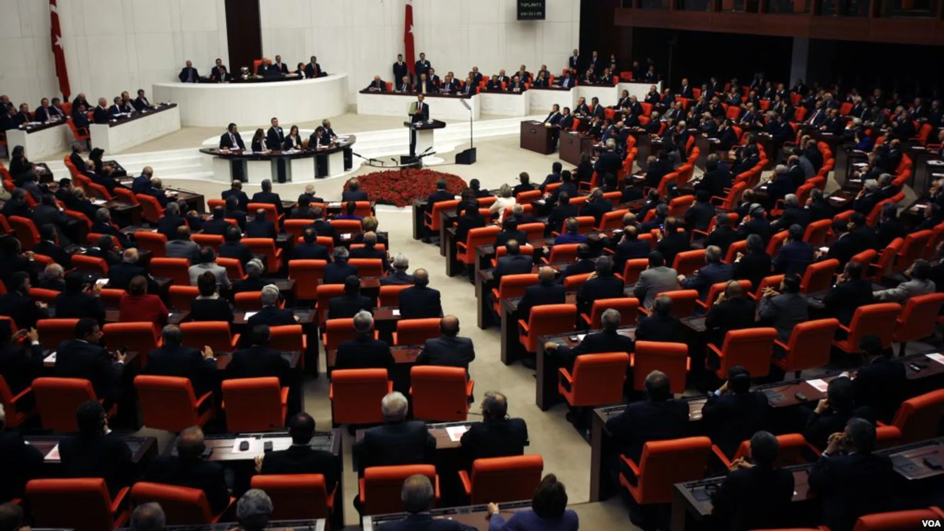 Turuncu koltuklarda oturan milletvekilleriyle dolu genel kurul salonu, ortada kürsüde konuşan bir kişi