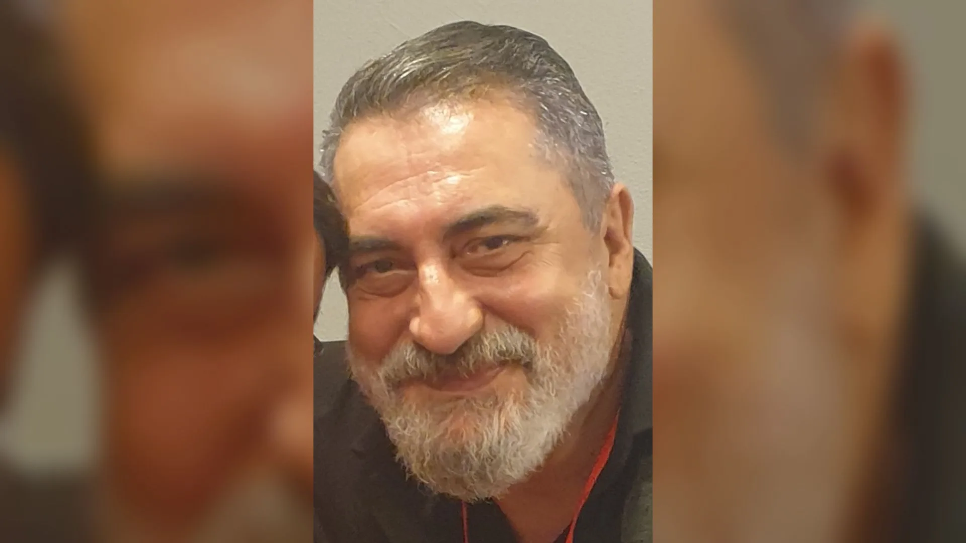 Kır saçlı, beyaz sakallı, siyah gömlekli gülümseyen bir adamın yakın portresi