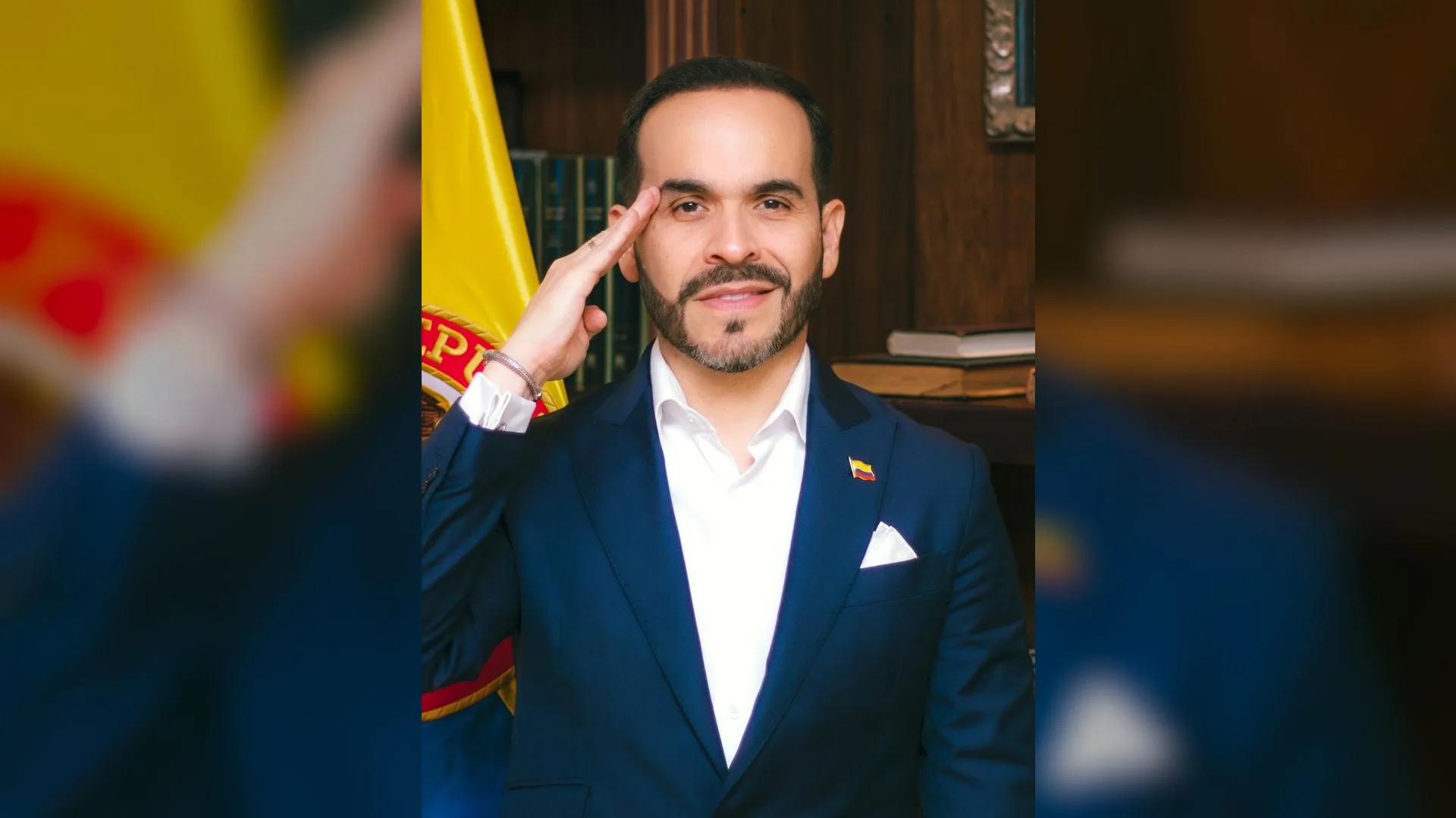 Kolombiya bayrağı önünde asker selamı veren sakallı, lacivert ceketli bir adam