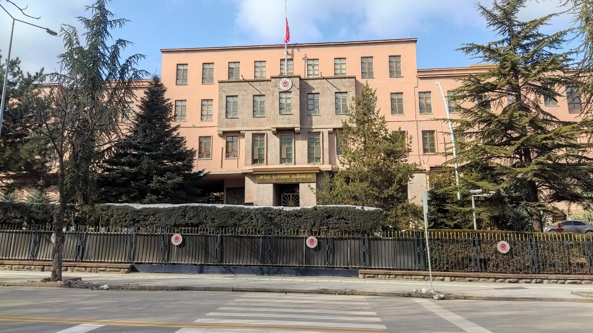 Çam ağaçları arasında, bayrağı yarıya inik pembe cepheli Milli Savunma Bakanlığı binası
