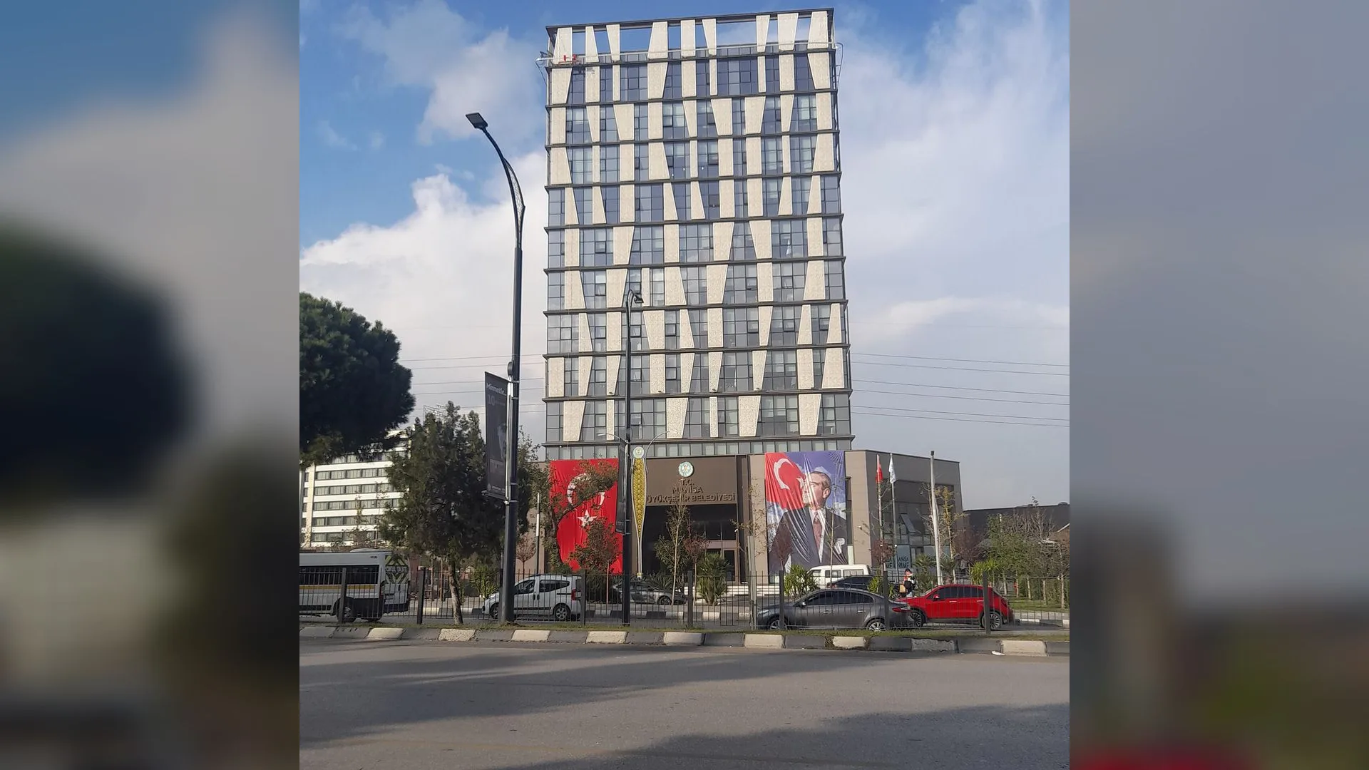 Önünde Türk bayrağı ve Atatürk posteri asılı, beyaz desenli cepheye sahip yüksek bir bina