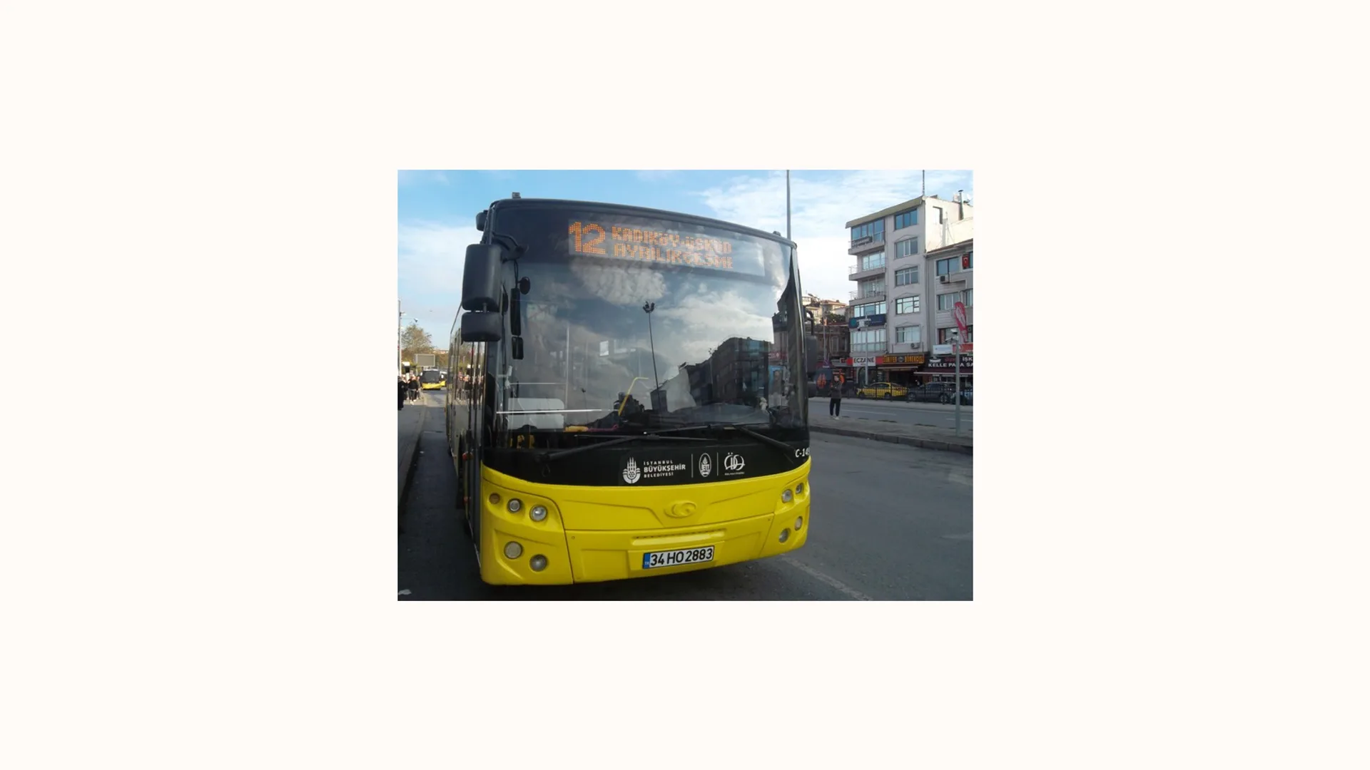 Şehir caddesinde duran, ön camında hat tabelası olan sarı belediye otobüsü