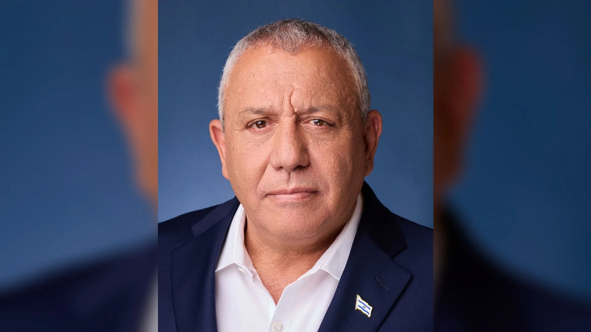 Lacivert ceketli, beyaz gömlekli, kır saçlı bir adamın mavi fonda portresi