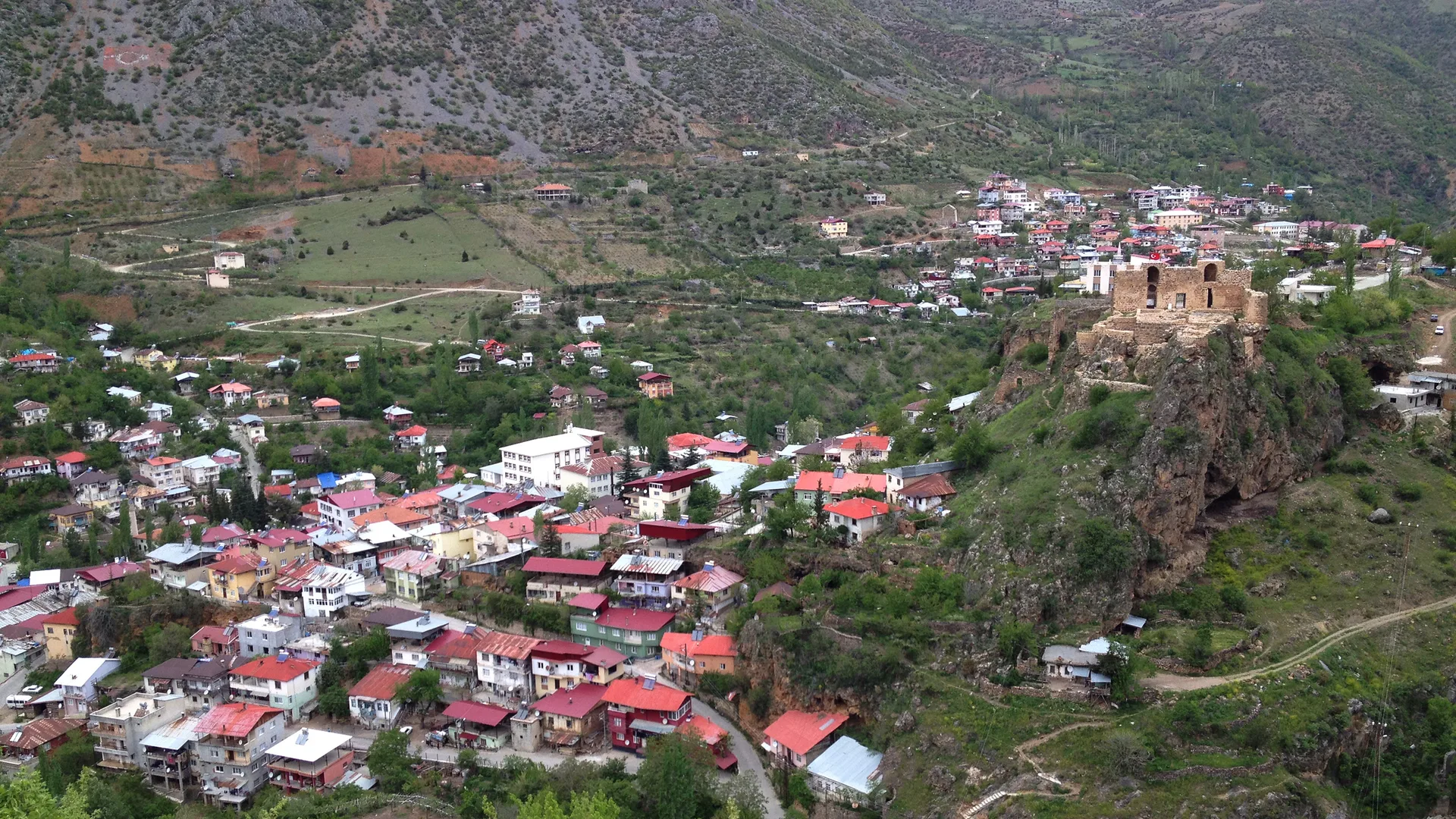 Dağ eteğindeki kırmızı çatılı evler ve kayalık tepedeki eski kale kalıntısı