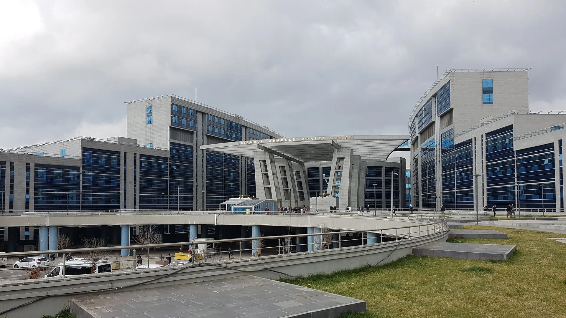 Bulutlu havada çimenlik alanın ardında cam cepheli büyük adliye binaları