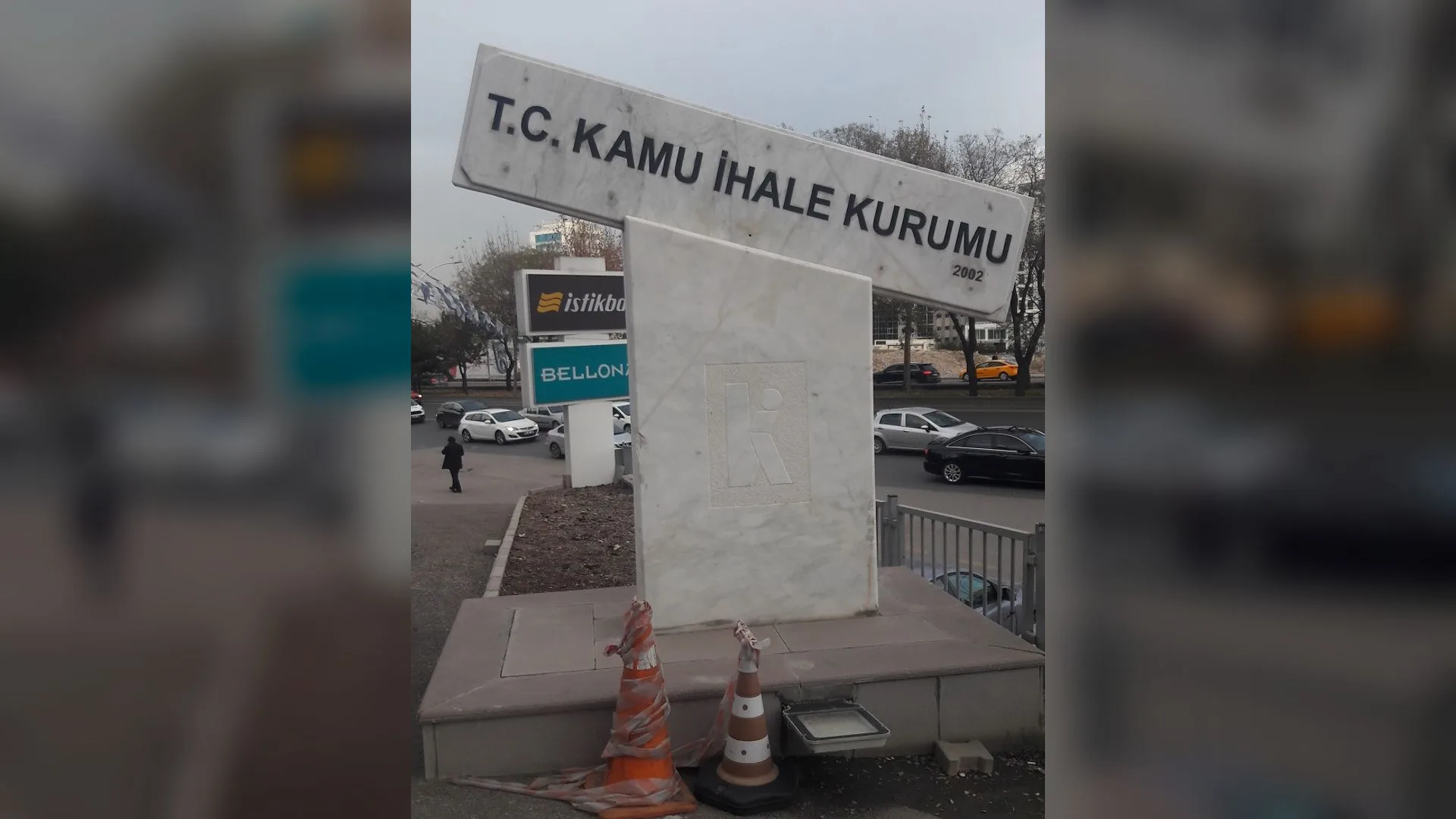 Yol kenarında "T.C. Kamu İhale Kurumu" yazılı mermer tabela, önünde turuncu trafik konileri