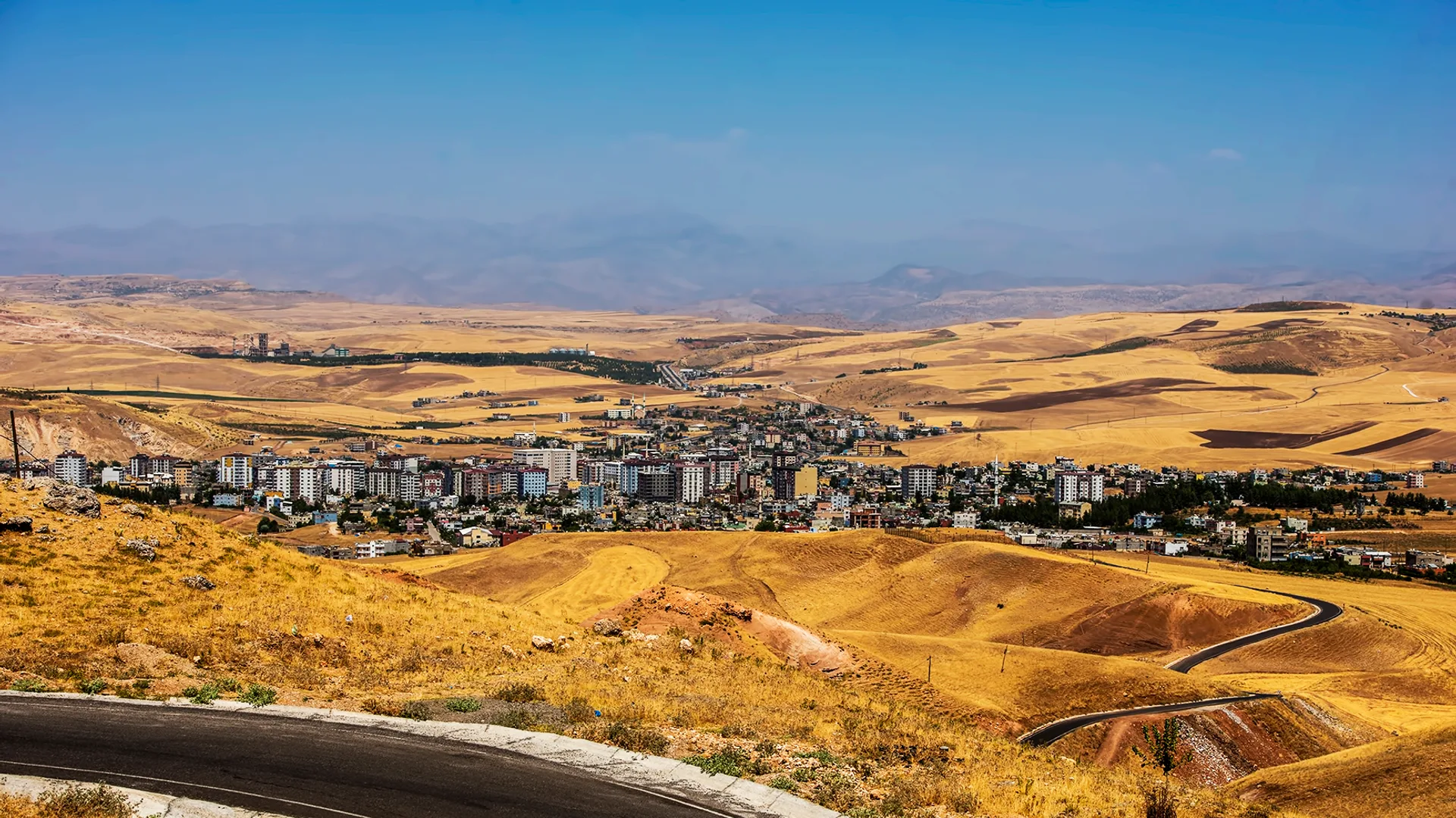 Sarı tepeler arasına kurulmuş bir ilçe ve önde kıvrılan asfalt yol