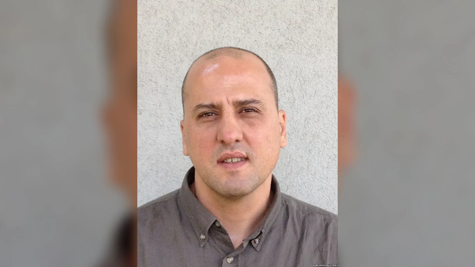Gri duvar önünde haki gömlekli, kısa saçlı bir adamın portresi