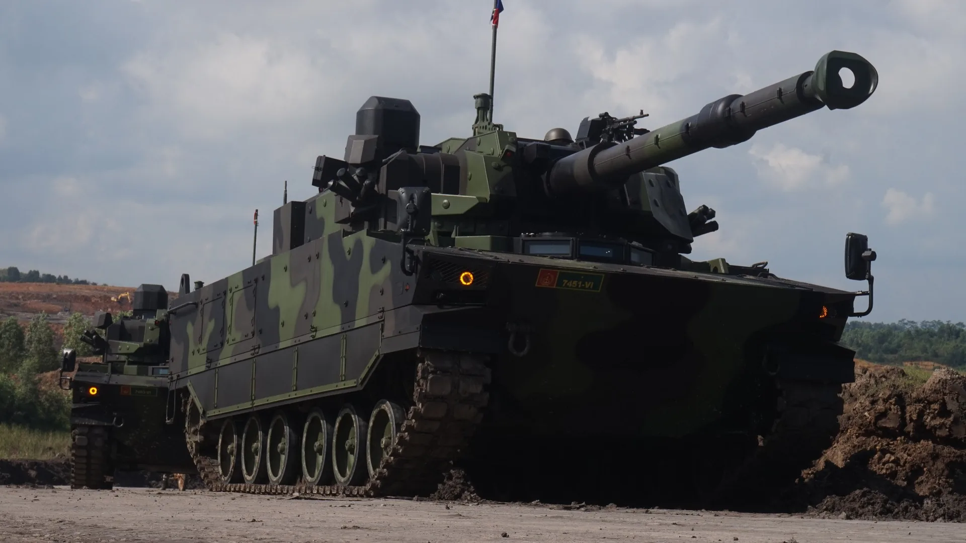 Bulutlu gökyüzü altında, toprak arazide duran kamuflaj boyalı bir tank