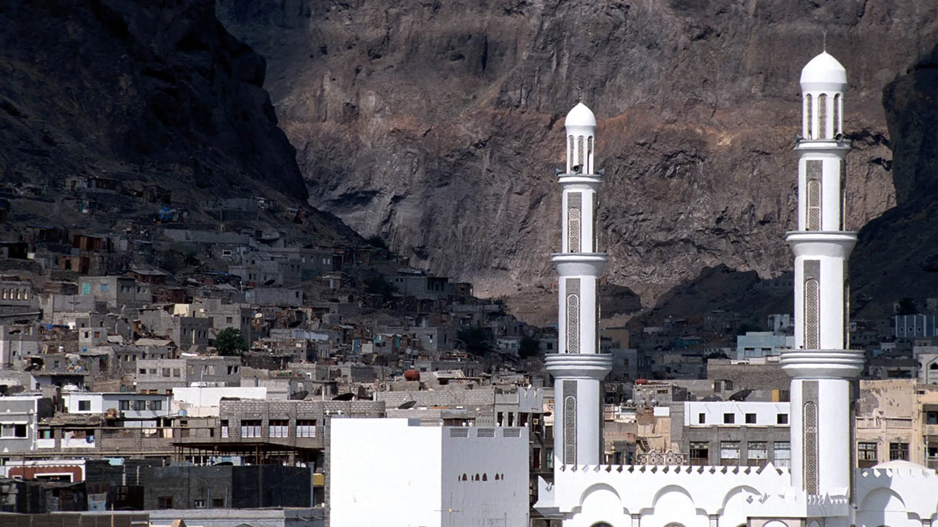 Kayalık dağların önünde yamaca yayılmış evler ve iki beyaz minareli cami