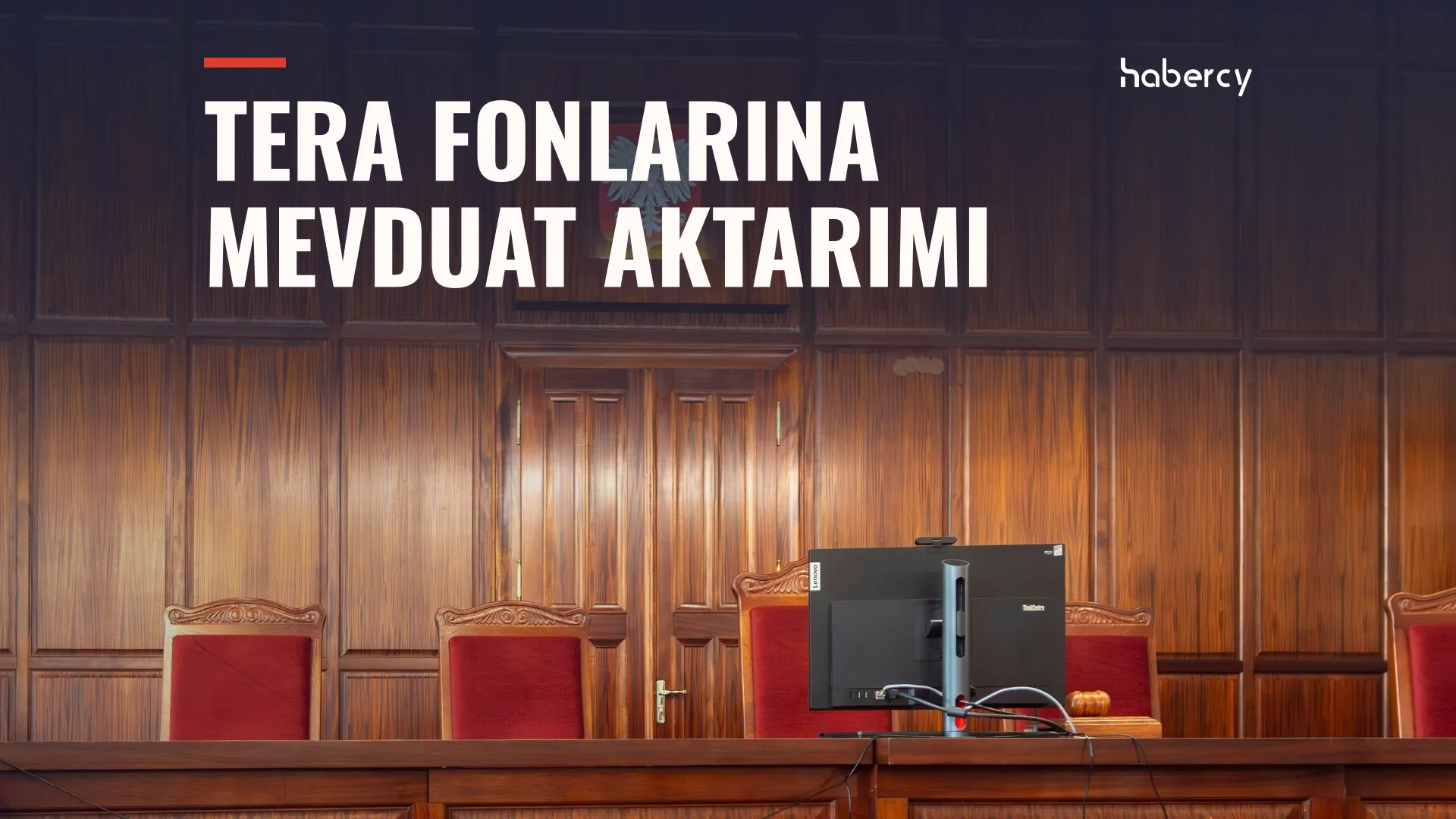 Ahşap kaplı boş bir mahkeme salonunda kırmızı koltuklar ve kürsüde bir bilgisayar ekranı