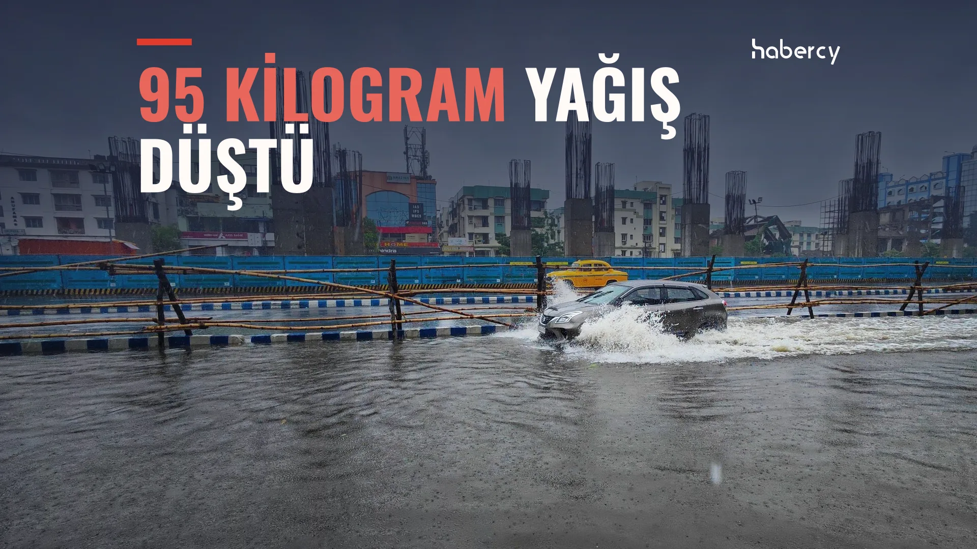 Sular altındaki yolda su sıçratarak ilerleyen gri otomobil, arkada inşaat kolonları