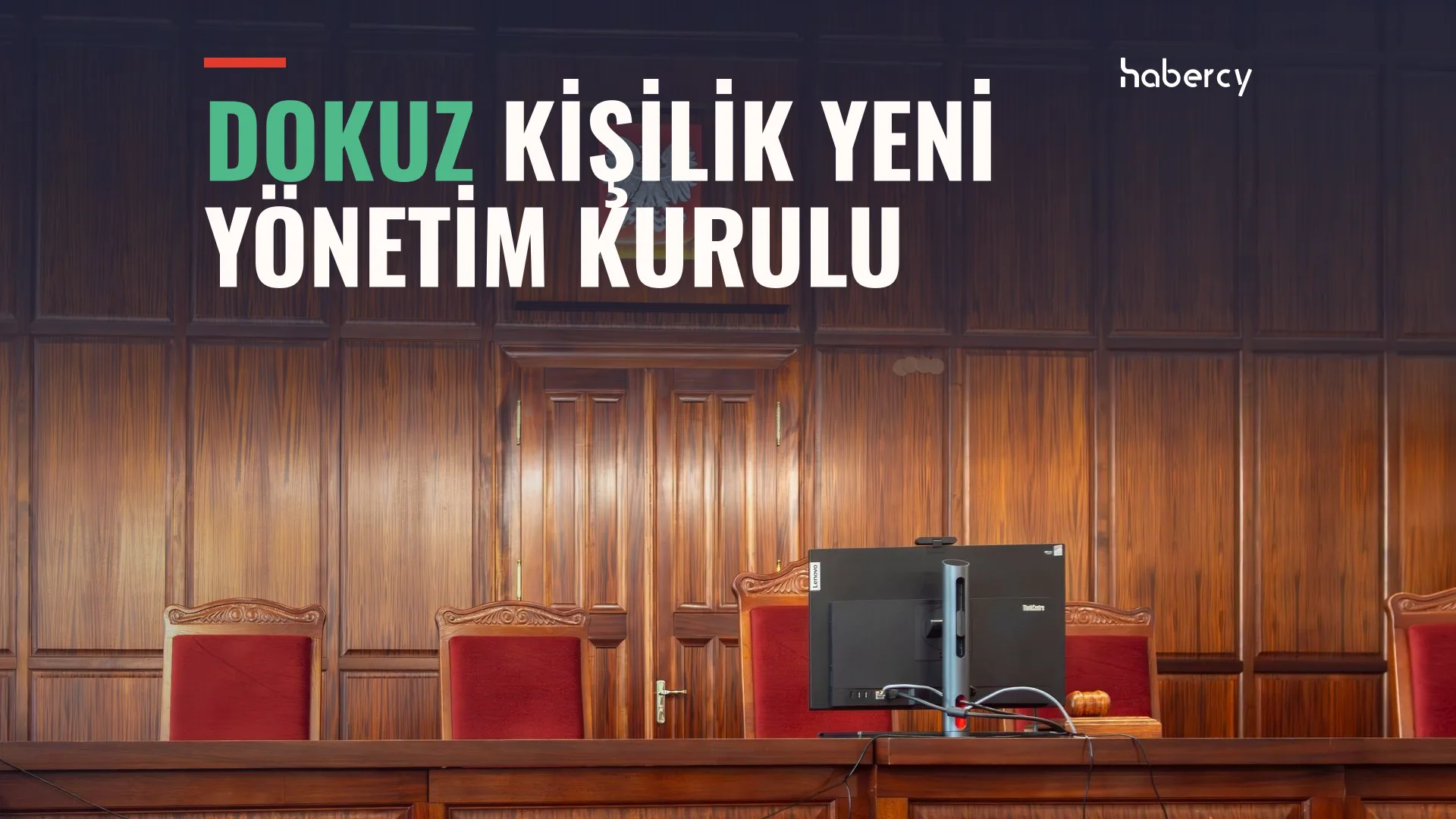 Ahşap kaplı salonda kırmızı koltuklar ve kürsüde bir bilgisayar ekranı