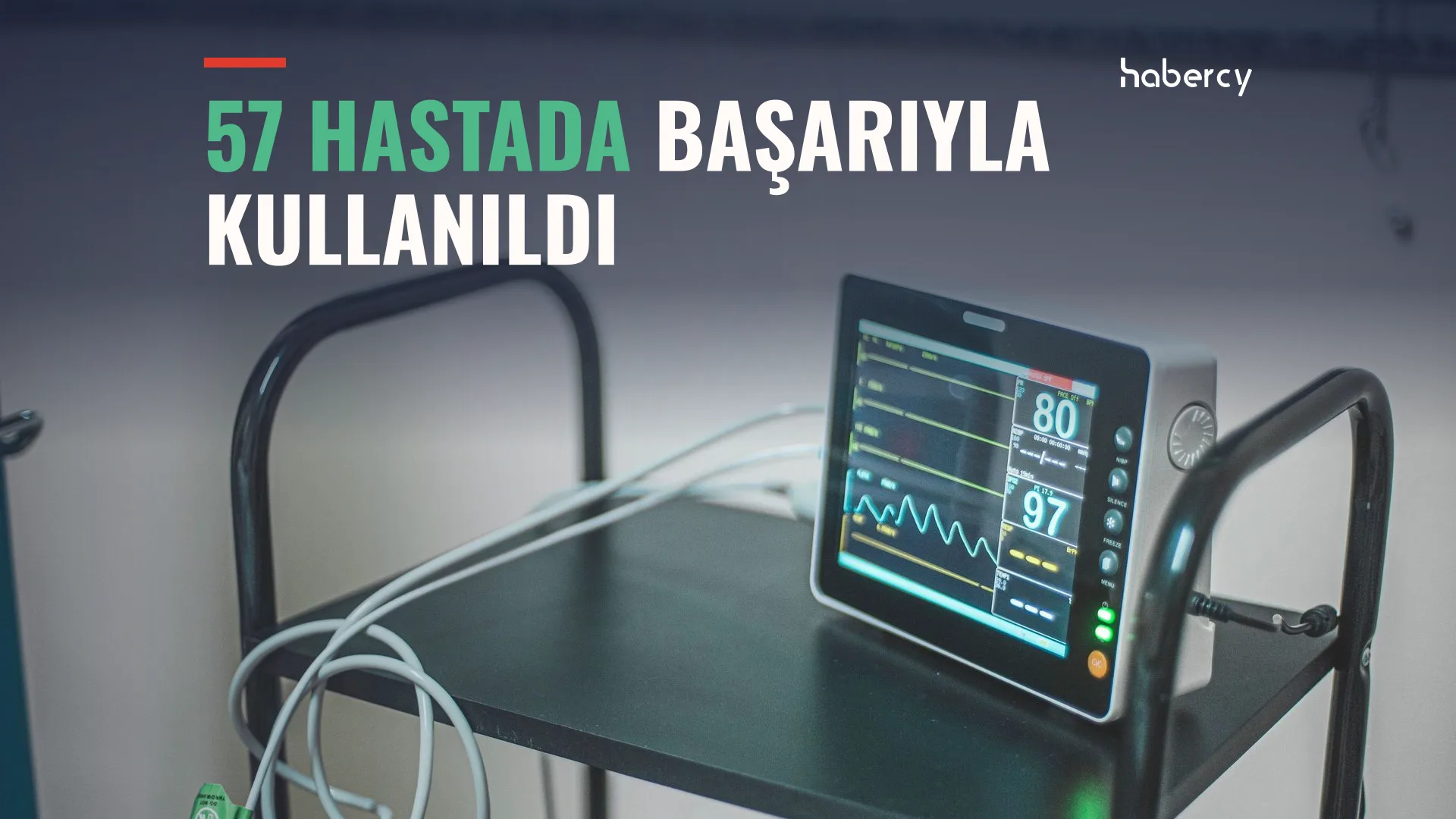 Siyah bir sehpanın üzerinde kablolu, ekranında dalga grafikleri ve değerler görünen hasta monitörü