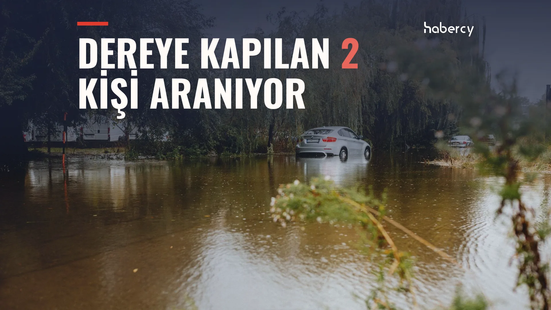 Ağaçlarla çevrili, kahverengi sel suyuyla dolmuş bir alanda yarıya kadar suya gömülmüş beyaz bir otomobil